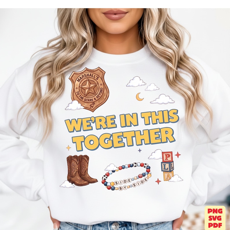 Op de afbeelding: Een wit sweatshirt met ronde hals en een grafische print met een bruine sheriff-badge, cowboylaarzen, een kralenarmband met de tekst SIDE BY SIDE en alfabetblokken. De tekst WE'RE IN THIS TOGETHER is in het geel op de voorzijde gedrukt.