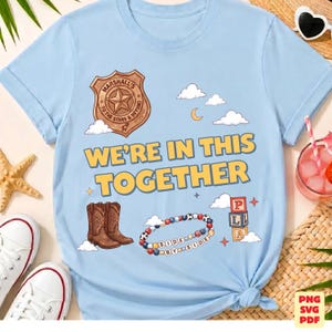 Op de afbeelding: Een lichtblauw t-shirt met een grafische print van een sheriff-badge met de tekst Marshall's To The Stars & Beyond, de tekst We're In This Together, een paar bruine cowboylaarzen, een kralenarmband en speelgoedblokken.