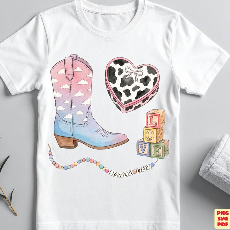 May include: A white t-shirt featuring a watercolor-style graphic of a cowboy boot with a pink and blue cloud pattern, a heart-shaped box with a black and white cow print, three stacked alphabet blocks, and a string of beads spelling LOVER BOY.