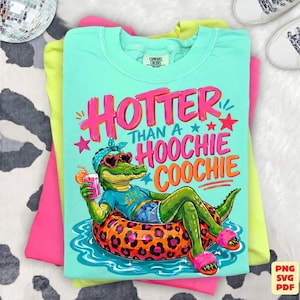 May include: A turquoise Comfort Colors t-shirt with a graphic of an alligator wearing sunglasses and a headband, lounging on an inflatable ring. The text reads "Hotter Than a Hoochie Coochie". The shirt is stacked with other brightly colored shirts.