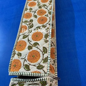 May include: A long, rectangular, quilted fabric case featuring a cream background with an orange floral pattern and green leaves. The edges are finished with a green and white striped trim, and a metal zipper is visible at the bottom with Bagru Exports text.