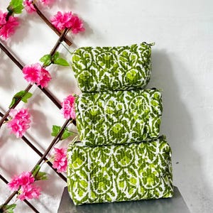 Puede incluir: Una pila de tres estuches rectangulares acolchados de diferentes tamaños, con un estampado floral en blanco y verde. Cada estuche cuenta con un cierre de cremallera y una textura suave y acolchada con costuras visibles en toda la superficie.
