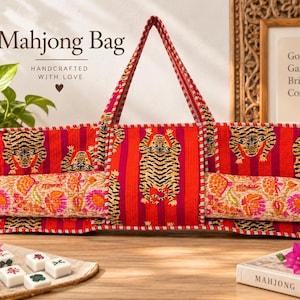 Puede incluir: Un bolso rectangular de tela para Mahjong con un vibrante patrón de rayas rojas y rosas e ilustraciones repetidas de tigres negros y amarillos. El bolso incluye dos asas superiores y un bolsillo frontal horizontal con un estampado floral.
