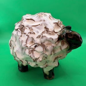 May include: A ceramic sheep figurine featuring a glossy white, textured wool body with brown accents in the crevices. The head and legs are finished in a dark, smooth brown glaze, creating a contrast with the lighter, uneven surface of the wool.