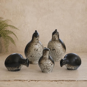 May include: A collection of five ceramic bird figurines in varying sizes. Two larger birds feature a speckled cream and black glaze, while three smaller birds are finished in a solid glossy black with subtle grey-toned speckling at the base.