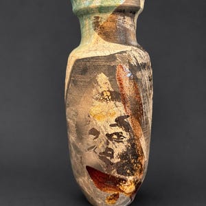 May include: A ceramic vase with a cylindrical body and a flared rim, featuring a textured surface with abstract brushstrokes in shades of brown, black, cream, and muted green, displaying a weathered appearance with visible clay variations.