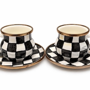 May include: Two ceramic teacups and saucers. The cups and saucers have a black and white checkered pattern. The rims of the cups and saucers are trimmed with gold. The cups have white handles.