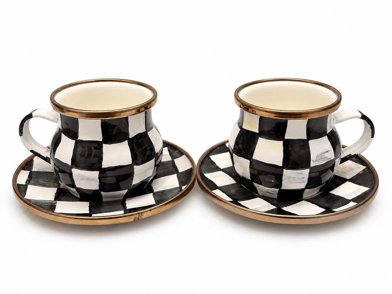 May include: Two ceramic teacups and saucers. The cups and saucers have a black and white checkered pattern. The rims of the cups and saucers are trimmed with gold. The cups have white handles.