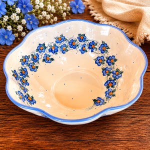 May include: A ceramic serving bowl with a scalloped edge and a cream-colored interior. The bowl is decorated with blue floral patterns and a blue rim. The bowl is approximately 12 inches in diameter.