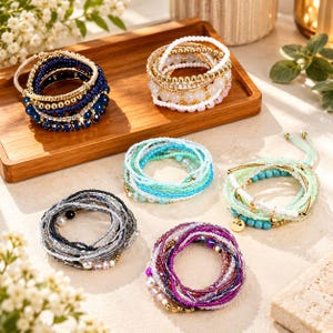 May include: Six multi-layered beaded bracelets in various color palettes including deep blue, white and gold, light turquoise, mint green, grey and black, and purple and pink. Each bracelet features small glass beads and metallic accents.