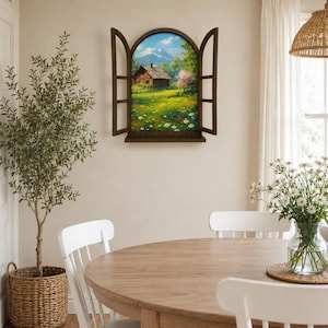 Puede incluir: Un marco decorativo de pared con forma de ventana arqueada y contraventanas abiertas, que muestra un paisaje pintado de una cabaña de madera en un prado con flores, árboles verdes y una montaña nevada bajo un cielo azul.
