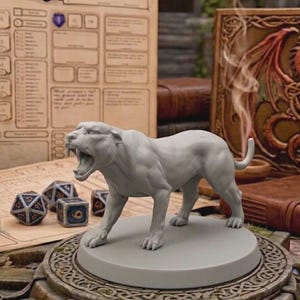 Könnte beinhalten: Graue, brüllende Pantherfigur, wahrscheinlich für Tabletop-Spiele. Würfel und ein Charakterbogen sind zu sehen, zusammen mit einem Buch mit einer Drachenillustration. Die Figur ist detailliert und scheint aus Harz oder einem ähnlichen Material zu bestehen.