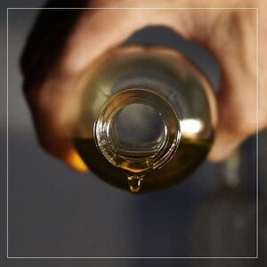 May include: A clear glass bottle with a golden liquid inside is being poured, with a single drop of liquid falling from the bottle's opening.