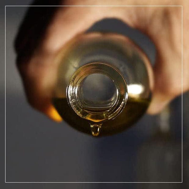 May include: A clear glass bottle with a golden liquid inside is being poured, with a single drop of liquid falling from the bottle's opening.