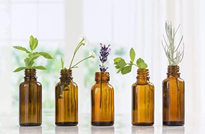 May include: Five amber glass bottles with droppers, each containing a different type of essential oil. The bottles are arranged in a row on a white surface. The oils are labeled with different herbs and flowers, including mint, lavender, and chamomile.