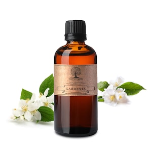 May include: A brown glass bottle with a black cap filled with Gardenia essential oil. The bottle has a brown paper label with the text "Nature's Note Organics 100% Pure Aromatherapy Gardenia" and a website address. White gardenia flowers are on the left and right sides of the bottle.