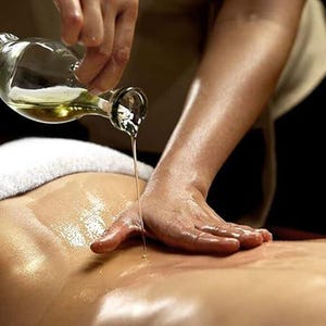 May include: A person's hand pours oil from a clear glass bottle onto a person's back during a massage.