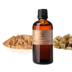 Könnte beinhalten: Eine braune Glasflasche mit schwarzem Verschluss, beschriftet mit "Nature's Note Organic 100% Pure Aromatherapy Essential Oil Frankincense & Myrrh naturesnoteorganics.com". Die Flasche steht auf einem weißen Hintergrund mit zwei Haufen braunem Harz davor.