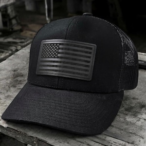 May include: Black trucker hat with a black and white American flag patch on the front.