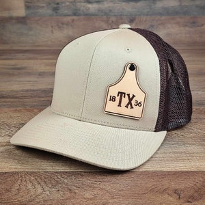 May include: A beige and brown trucker hat with a leather patch that says "18 TX 36".