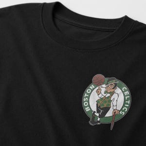 May include: Black t-shirt with the Boston Celtics logo. The logo shows a leprechaun with a basketball, within a green and white circular design with the words "BOSTON CELTICS".