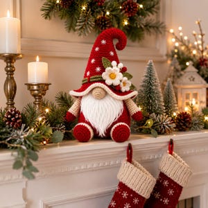 May include: A crochet gnome figurine featuring a tall red pointed hat with white snowflake embroidery, a long white beard, and a beige nose. The hat is decorated with white fabric flowers and green leaves. The gnome has red arms and feet.