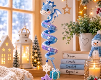 Peut inclure: Une décoration en crochet en forme de spirale représentant un dragon dans des tons bleu et violet, avec une tête de dragon en haut, des étoiles blanches, un flocon de neige, une étoile violette souriante et un petit cadeau bleu suspendu.