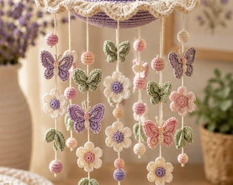 May include: A hanging mobile featuring crocheted elements including lavender, pink, and green butterflies, white flowers with purple centres, and a central rainbow with white clouds at the base. The structure is suspended from a lavender crocheted dome.