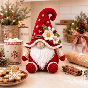May include: A crocheted gnome figurine featuring a tall, pointed red hat decorated with white snowflake embroidery and a cluster of white flowers with green leaves. The gnome has a beige nose, a long white beard, and red crocheted feet.