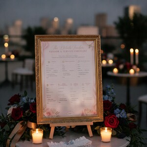 May include: A gold ornate frame holds a printed vendor and service checklist titled The Details Tracker. The sign sits on a wooden easel surrounded by red roses, blue flowers, two lit candles, a white lace garter, and a small beaded accessory.
