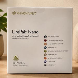 Pharmanex LifePak Nano dietary supplement box placed on a wooden table in a minimalist home setting with soft lighting, indoor plant decor, framed wall art, and a ceramic vase in the background.