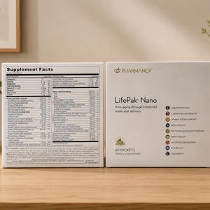 Two Pharmanex LifePak Nano supplement boxes displayed on a wooden table in a modern home-style setup with decorative plants, books, soft beige wall background, and natural indoor lighting.
