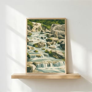 May include: A framed print of a cascading waterfall scene. The artwork depicts water flowing over rocks, with green foliage at the top. The print is in a wooden frame and rests on a wooden shelf.