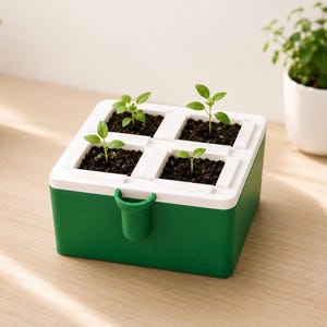 Puede incluir: Una jardinera cuadrada verde y blanca con cuatro secciones individuales, cada una llena de tierra y pequeñas plantas verdes. La jardinera tiene un asa en la parte delantera. Una pequeña maceta blanca con una planta verde está en el fondo.
