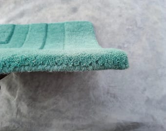 Puede incluir: Una alfombrilla de baño rectangular de color verde menta con una textura de pelo grueso y copetudo con crestas horizontales paralelas en la superficie. La alfombrilla tiene una construcción densa y suave con un reverso de tela visible.