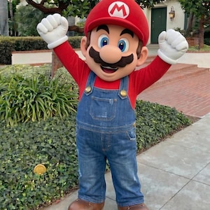 Puede incluir: Una persona con un disfraz de Mario, con un gorro rojo con una "M" blanca, una camisa roja de manga larga, un peto vaquero azul y zapatos marrones. El personaje tiene un gran bigote y guantes blancos, con los brazos levantados.