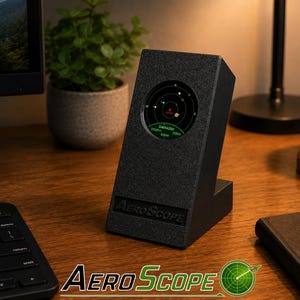 Könnte beinhalten: Ein schwarzes, angewinkeltes Tischgerät mit der Aufschrift AeroScope und einem runden Digitaldisplay, das eine Radarschnittstelle zeigt. Der Bildschirm verfügt über ein grünes kreisförmiges Gitter mit verschiedenen Datenpunkten, inklusive SWA4250 und 70km.
