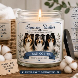 Op de afbeelding: Een geurkaars "Clean Cotton" in een glazen pot. Het etiket toont drie Sheltie-hondenportretten en de tekst "Legacies Shelties". Tekst: "Gemaakt met 100% natuurlijke sojawas" en "Handgegoten in de VS". De kaars is 9oz.