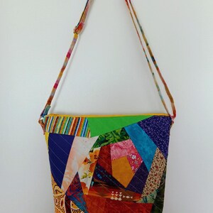 May include: A crossbody bag featuring a vibrant patchwork design made from various fabric scraps in shades of yellow, green, blue, purple, and orange. The bag has a yellow zipper closure and an adjustable shoulder strap with a multicolored pattern.