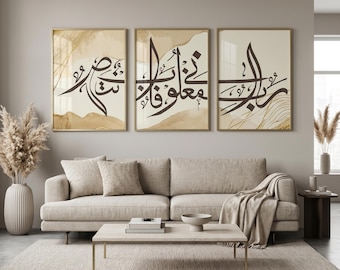 May include: Three framed art prints with Arabic calligraphy in a living room setting. The prints feature brown calligraphy on a beige background with gold accents. The frames are gold, and the artwork is displayed above a beige sofa.