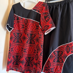 May include: A two-piece set consisting of a short-sleeved top and a skirt. Both pieces feature a black and red geometric pattern with white piping accents. The top has a solid black upper section, while the skirt has a solid black upper portion.
