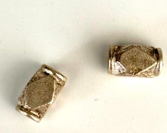 May include: Two small, silver-colored metal beads. Each bead is a short cylinder with a diamond-shaped pattern on the sides. The beads are slightly tarnished, giving them a vintage appearance. They are set against a white background.