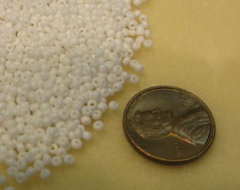 May include: A large pile of white seed beads, next to a UK penny for scale.