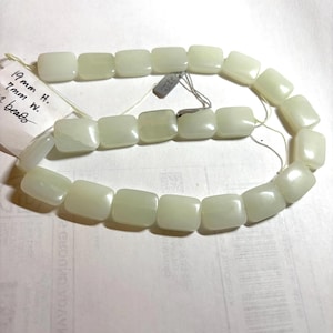 May include: A strand of pale green, rectangular beads. The beads are strung together on a thin, off-white string. A tag attached to the strand indicates the beads are 19mm high and 7mm wide. The beads have a slightly translucent appearance.