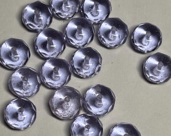 May include: A collection of small, round, translucent light purple buttons with a faceted, multi-sided edge design. Each button features a central shank on the underside for attachment, showcasing a clear, glass-like appearance.