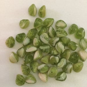 May include: A pile of green and white swirl glass beads. The beads are shaped like seashells and have a glossy finish.