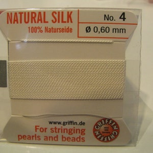 May include: A white spool of natural silk thread for stringing pearls and beads. The spool is labeled "NATURAL SILK 100% Naturseide No. 4 Ø 0,60 mm" and "www.griffin.de For stringing pearls and beads".