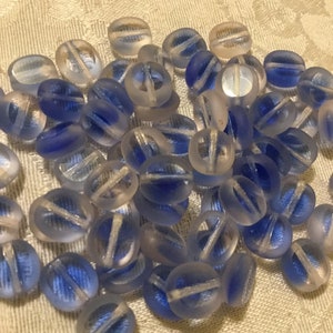 May include: A pile of translucent blue glass beads with a white stripe running through the center of each bead.