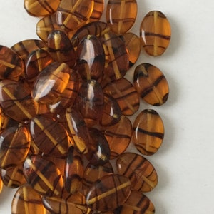 May include: A pile of oval-shaped glass beads with a brown and gold striped pattern.