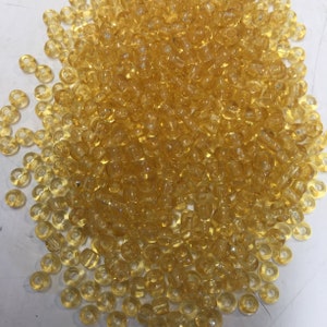 May include: A large pile of small, translucent, amber-colored glass beads. The beads are round with a hole in the center.